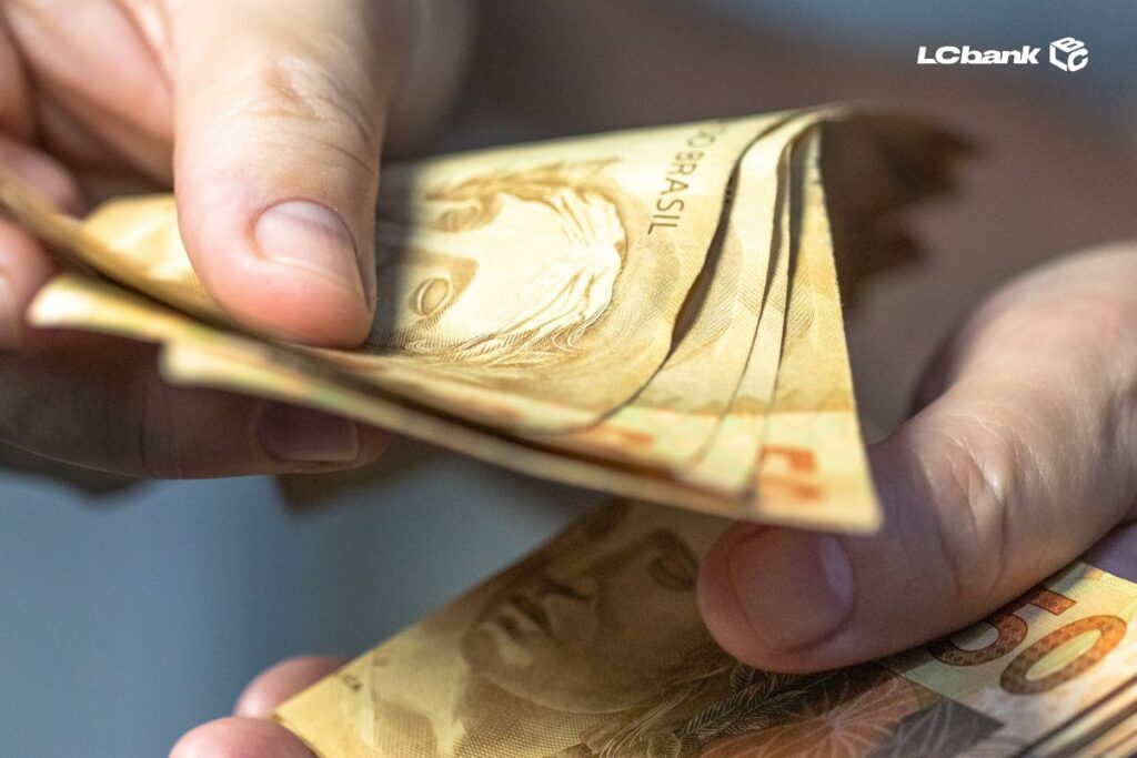 Imagem de notas de cinquenta reais e uma pessoa contando os valores