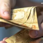 Imagem de notas de cinquenta reais e uma pessoa contando os valores